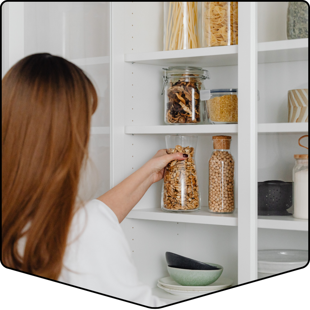 Person reaching into a white pantry with shelves stocked with jars and containers.